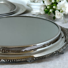 Vintage Sheffield Silver Co. Shrewsbury Plateau round silver-plated tray with mirrored surface and ornate floral scrollwork border; footed design with four decorative legs; shown outdoors with sky and leaves reflected in mirror; very good vintage condition with original packaging and maker’s sticker from Norton, Massachusetts.