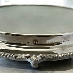 Vintage Sheffield Silver Co. Shrewsbury Plateau round silver-plated tray with mirrored surface and ornate floral scrollwork border; footed design with four decorative legs; shown outdoors with sky and leaves reflected in mirror; very good vintage condition with original packaging and maker’s sticker from Norton, Massachusetts.