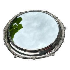 Vintage Sheffield Silver Co. Shrewsbury Plateau round silver-plated tray with mirrored surface and ornate floral scrollwork border; footed design with four decorative legs; shown outdoors with sky and leaves reflected in mirror; very good vintage condition with original packaging and maker’s sticker from Norton, Massachusetts.