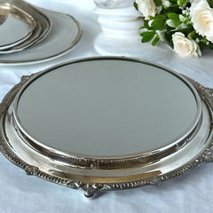 Vintage Sheffield Silver Co. Shrewsbury Plateau round silver-plated tray with mirrored surface and ornate floral scrollwork border; footed design with four decorative legs; shown outdoors with sky and leaves reflected in mirror; very good vintage condition with original packaging and maker’s sticker from Norton, Massachusetts.