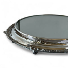 Vintage Sheffield Silver Co. Shrewsbury Plateau round silver-plated tray with mirrored surface and ornate floral scrollwork border; footed design with four decorative legs; shown outdoors with sky and leaves reflected in mirror; very good vintage condition with original packaging and maker’s sticker from Norton, Massachusetts.