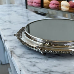 Vintage Sheffield Silver Co. Shrewsbury Plateau round silver-plated tray with mirrored surface and ornate floral scrollwork border; footed design with four decorative legs; shown outdoors with sky and leaves reflected in mirror; very good vintage condition with original packaging and maker’s sticker from Norton, Massachusetts.
