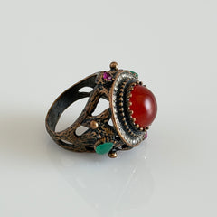 Vintage 1990s Turkish Sultan‑style brass ring with ornate beadwork and cut‑outs, featuring a central carnelian‑colored glass cabochon surrounded by green, ruby, and clear rhinestones on an antique brass setting.