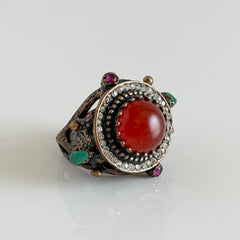 Vintage 1990s Turkish Sultan‑style brass ring with ornate beadwork and cut‑outs, featuring a central carnelian‑colored glass cabochon surrounded by green, ruby, and clear rhinestones on an antique brass setting.