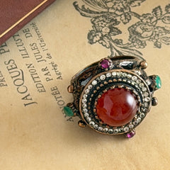 Vintage 1990s Turkish Sultan‑style brass ring with ornate beadwork and cut‑outs, featuring a central carnelian‑colored glass cabochon surrounded by green, ruby, and clear rhinestones on an antique brass setting.