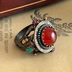 Vintage 1990s Turkish Sultan‑style brass ring with ornate beadwork and cut‑outs, featuring a central carnelian‑colored glass cabochon surrounded by green, ruby, and clear rhinestones on an antique brass setting.