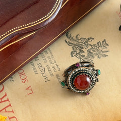 Vintage 1990s Turkish Sultan‑style brass ring with ornate beadwork and cut‑outs, featuring a central carnelian‑colored glass cabochon surrounded by green, ruby, and clear rhinestones on an antique brass setting.