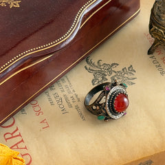 Vintage 1990s Turkish Sultan‑style brass ring with ornate beadwork and cut‑outs, featuring a central carnelian‑colored glass cabochon surrounded by green, ruby, and clear rhinestones on an antique brass setting.