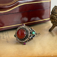Vintage 1990s Turkish Sultan‑style brass ring with ornate beadwork and cut‑outs, featuring a central carnelian‑colored glass cabochon surrounded by green, ruby, and clear rhinestones on an antique brass setting.