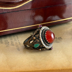 Vintage 1990s Turkish Sultan‑style brass ring with ornate beadwork and cut‑outs, featuring a central carnelian‑colored glass cabochon surrounded by green, ruby, and clear rhinestones on an antique brass setting.