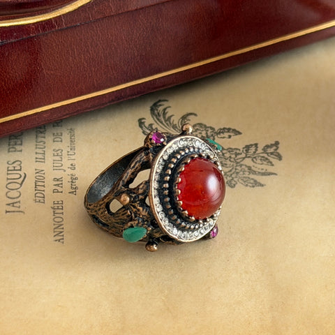 Vintage 1990s Turkish Sultan‑style brass ring with ornate beadwork and cut‑outs, featuring a central carnelian‑colored glass cabochon surrounded by green, ruby, and clear rhinestones on an antique brass setting.