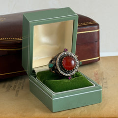 Vintage 1990s Turkish Sultan‑style brass ring with ornate beadwork and cut‑outs, featuring a central carnelian‑colored glass cabochon surrounded by green, ruby, and clear rhinestones on an antique brass setting.