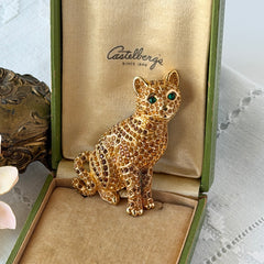 Vintage Swarovski cat brooch from the 1996 Precious Pets collection with hand‑polished gold‑plated setting, topaz and smoked topaz pavé crystals, green cabochon eyes, and honey‑brown enamel back, shown in various angles and lighting.