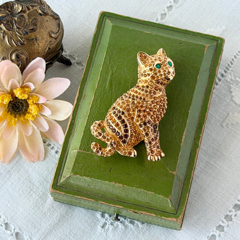 Vintage Swarovski cat brooch from the 1996 Precious Pets collection with hand‑polished gold‑plated setting, topaz and smoked topaz pavé crystals, green cabochon eyes, and honey‑brown enamel back, shown in various angles and lighting.