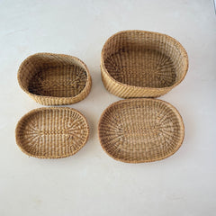 Two oval sweetgrass baskets with lids, hand‑woven in natural tones, shown nested together beside a white vase with flowers.