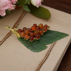 Vintage Swoboda brooch featuring a carved green jade leaf and a cluster of round carnelian berries set in gold‑tone metal, shown from multiple angles to highlight its details and signature.
