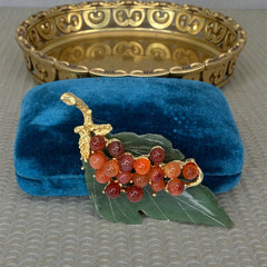 Vintage Swoboda brooch featuring a carved green jade leaf and a cluster of round carnelian berries set in gold‑tone metal, shown from multiple angles to highlight its details and signature.