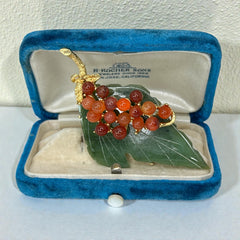 Vintage Swoboda brooch featuring a carved green jade leaf and a cluster of round carnelian berries set in gold‑tone metal, shown from multiple angles to highlight its details and signature.