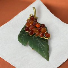 Vintage Swoboda brooch featuring a carved green jade leaf and a cluster of round carnelian berries set in gold‑tone metal, shown from multiple angles to highlight its details and signature.