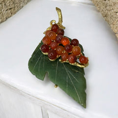Vintage Swoboda brooch featuring a carved green jade leaf and a cluster of round carnelian berries set in gold‑tone metal, shown from multiple angles to highlight its details and signature.