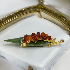 Vintage Swoboda brooch featuring a carved green jade leaf and a cluster of round carnelian berries set in gold‑tone metal, shown from multiple angles to highlight its details and signature.