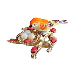 Vintage Swoboda bird nest brooch with a painted bone bird, faux pearl eggs, coral‑colored stone chips, and gold‑tone metal branch detailing.
