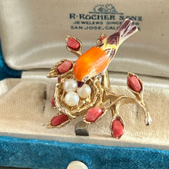 Vintage Swoboda bird nest brooch with a painted bone bird, faux pearl eggs, coral‑colored stone chips, and gold‑tone metal branch detailing.