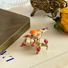 Vintage Swoboda bird nest brooch with a painted bone bird, faux pearl eggs, coral‑colored stone chips, and gold‑tone metal branch detailing.