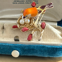 Vintage Swoboda bird nest brooch with a painted bone bird, faux pearl eggs, coral‑colored stone chips, and gold‑tone metal branch detailing.