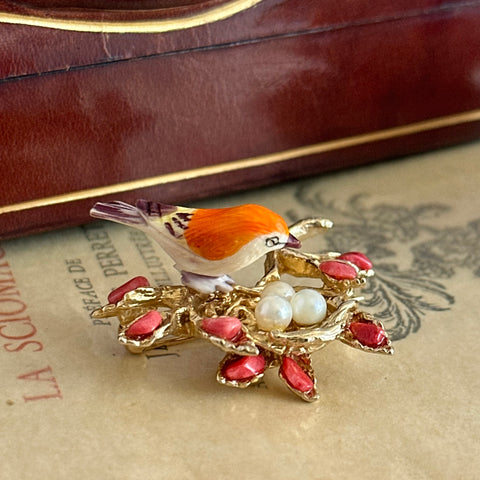 Vintage Swoboda bird nest brooch with a painted bone bird, faux pearl eggs, coral‑colored stone chips, and gold‑tone metal branch detailing.