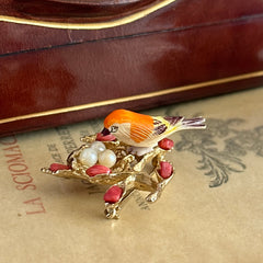 Vintage Swoboda bird nest brooch with a painted bone bird, faux pearl eggs, coral‑colored stone chips, and gold‑tone metal branch detailing.
