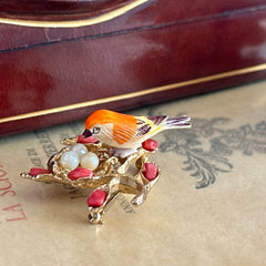 Vintage Swoboda bird nest brooch with a painted bone bird, faux pearl eggs, coral‑colored stone chips, and gold‑tone metal branch detailing.