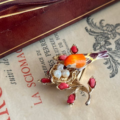 Vintage Swoboda bird nest brooch with a painted bone bird, faux pearl eggs, coral‑colored stone chips, and gold‑tone metal branch detailing.
