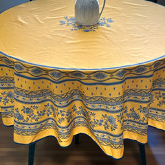 Round coated cotton tablecloth in sunny yellow and deep blue, featuring alternating Provençal floral and geometric bands