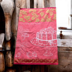 Pink French tea towel with golden strawberry leaves and a white illustration of a Charlotte aux Fraises dessert on a cake stand, by Coucke.