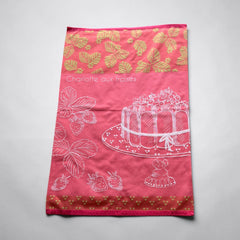 Pink French tea towel with golden strawberry leaves and a white illustration of a Charlotte aux Fraises dessert on a cake stand, by Coucke.
