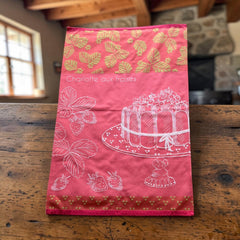Pink French tea towel with golden strawberry leaves and a white illustration of a Charlotte aux Fraises dessert on a cake stand, by Coucke.