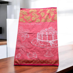 Pink French tea towel with golden strawberry leaves and a white illustration of a Charlotte aux Fraises dessert on a cake stand, by Coucke.