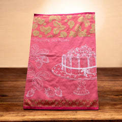 Pink French tea towel with golden strawberry leaves and a white illustration of a Charlotte aux Fraises dessert on a cake stand, by Coucke.