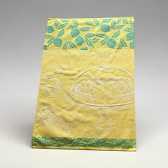 Yellow French tea towel with green lemon and leaf motifs and a white illustration of a lemon meringue tart on a cake stand, by Coucke.