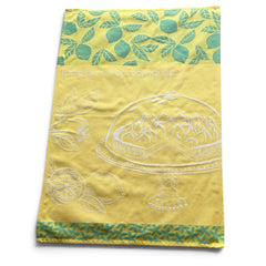 Yellow French tea towel with green lemon and leaf motifs and a white illustration of a lemon meringue tart on a cake stand, by Coucke.