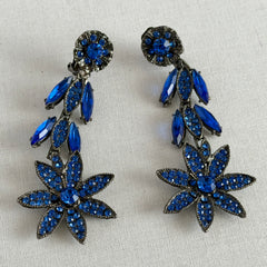 Pair of vintage 1980s Thelma Deutsch clip‑on earrings with deep blue rhinestones in a cascading dangle design set in dark gunmetal‑tone metal.