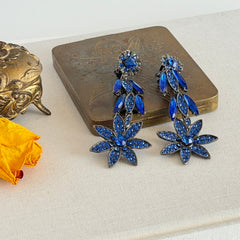 Pair of vintage 1980s Thelma Deutsch clip‑on earrings with deep blue rhinestones in a cascading dangle design set in dark gunmetal‑tone metal.