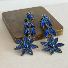 Pair of vintage 1980s Thelma Deutsch clip‑on earrings with deep blue rhinestones in a cascading dangle design set in dark gunmetal‑tone metal.