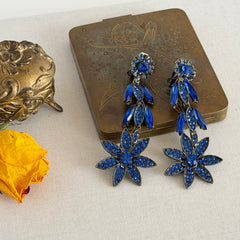 Pair of vintage 1980s Thelma Deutsch clip‑on earrings with deep blue rhinestones in a cascading dangle design set in dark gunmetal‑tone metal.