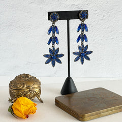 Pair of vintage 1980s Thelma Deutsch clip‑on earrings with deep blue rhinestones in a cascading dangle design set in dark gunmetal‑tone metal.