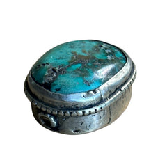 A vintage Tibetan 'silver' and turquoise bead from the 1990s, featuring a turquoise-green oval cabochon with natural matrix, set in a handcrafted bezel. The back of the bead displays intricate repousse work with swirling cloud and flower designs, iconic in Tibetan jewelry.