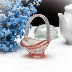 Vintage pink Depression glass favor basket with ruffled rim and twisted handle, styled on a neutral surface with soft natural light.