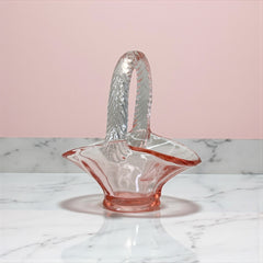 Vintage pink Depression glass favor basket with ruffled rim and twisted handle, styled on a neutral surface with soft natural light.