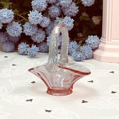 Vintage pink Depression glass favor basket with ruffled rim and twisted handle, styled on a neutral surface with soft natural light.